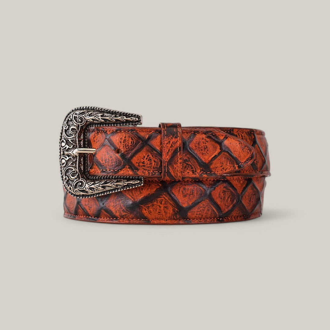 The Pirarucu Print Cogñac - Texas Buckle, a brown leather belt with a diamond pattern, is coiled neatly. It showcases an ornate silver buckle with intricate designs on a plain beige background.