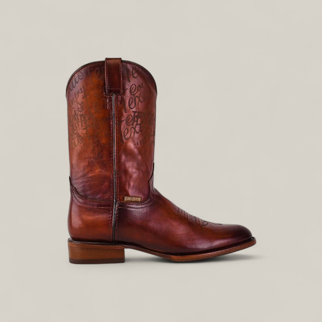 The Wyatt - Camel - Roper Toe boot features brown cowhide leather, a flat wooden heel, decorative stitching, and faint script text on the shaft, highlighting quality craftsmanship against a plain light background.