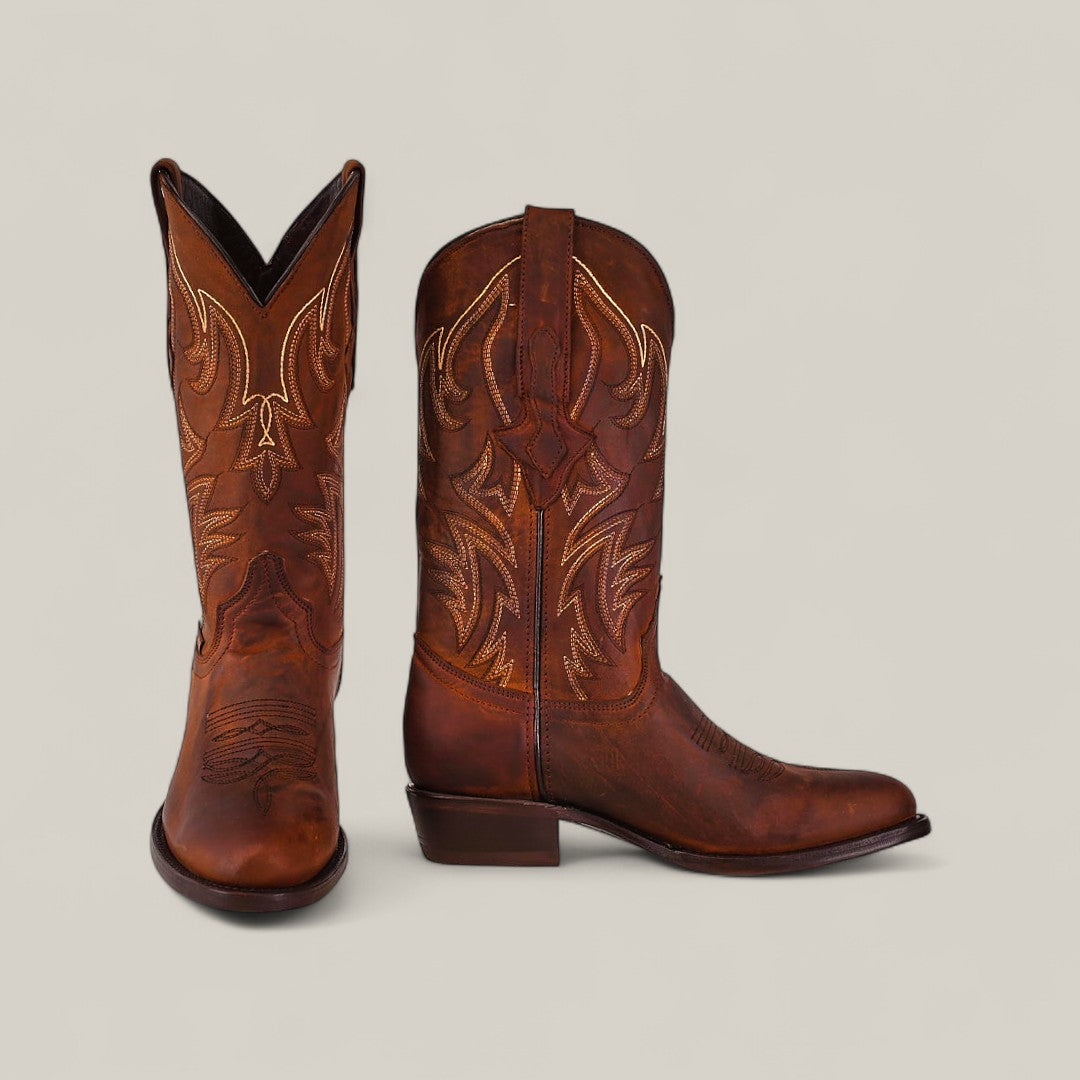 A pair of Dutton - Brick - Roper Toe boots in brown cowhide, featuring intricate light stitching, is displayed on a plain light backgroundāone boot facing forward, one from the sideāfrom the Last Call collection.