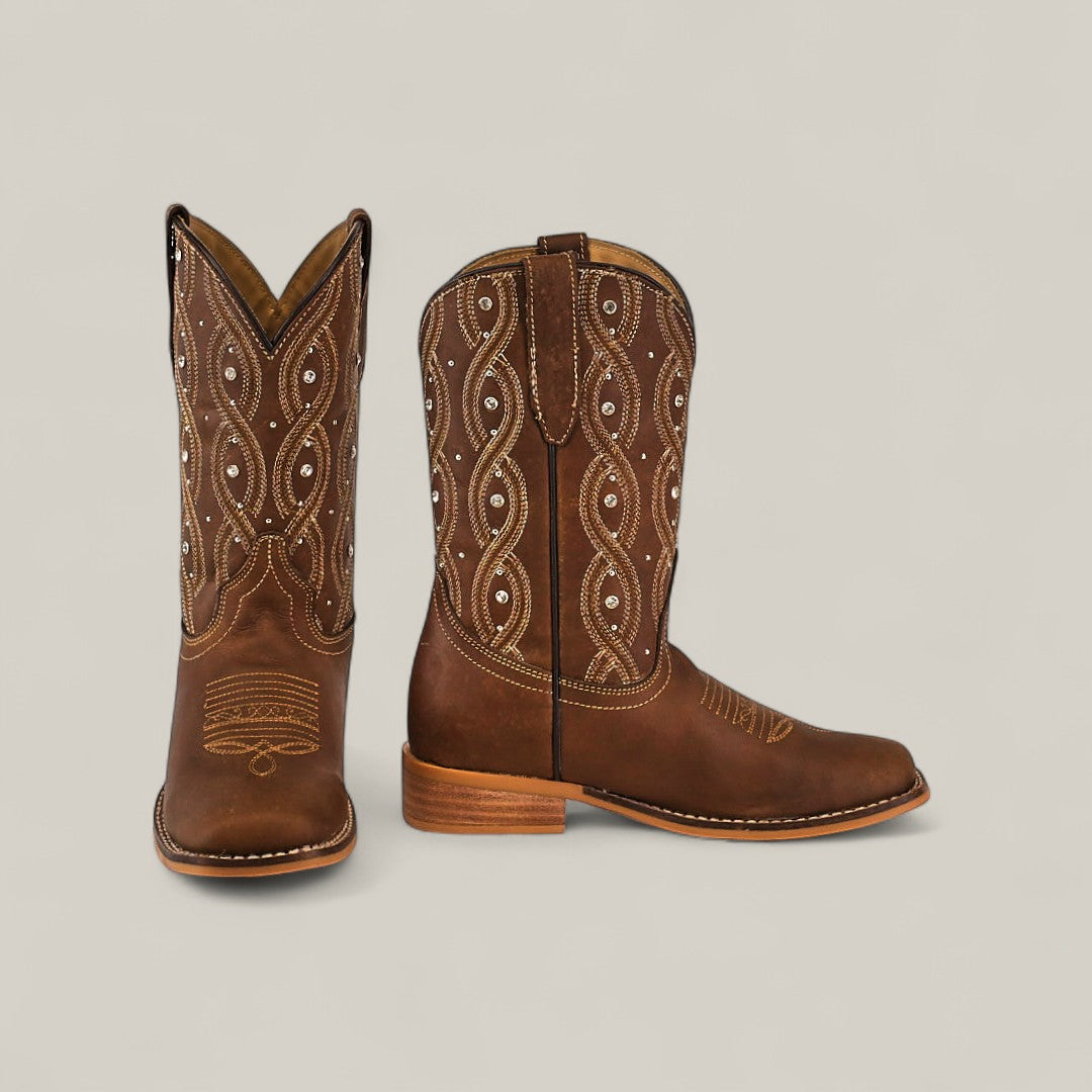 The Premiere Texas Copper - Square Toe Kids Boots feature brown leather with decorative white stitching and patterns, displayed on a plain light background for classic Texas style flair—one boot upright, the other sideways.
