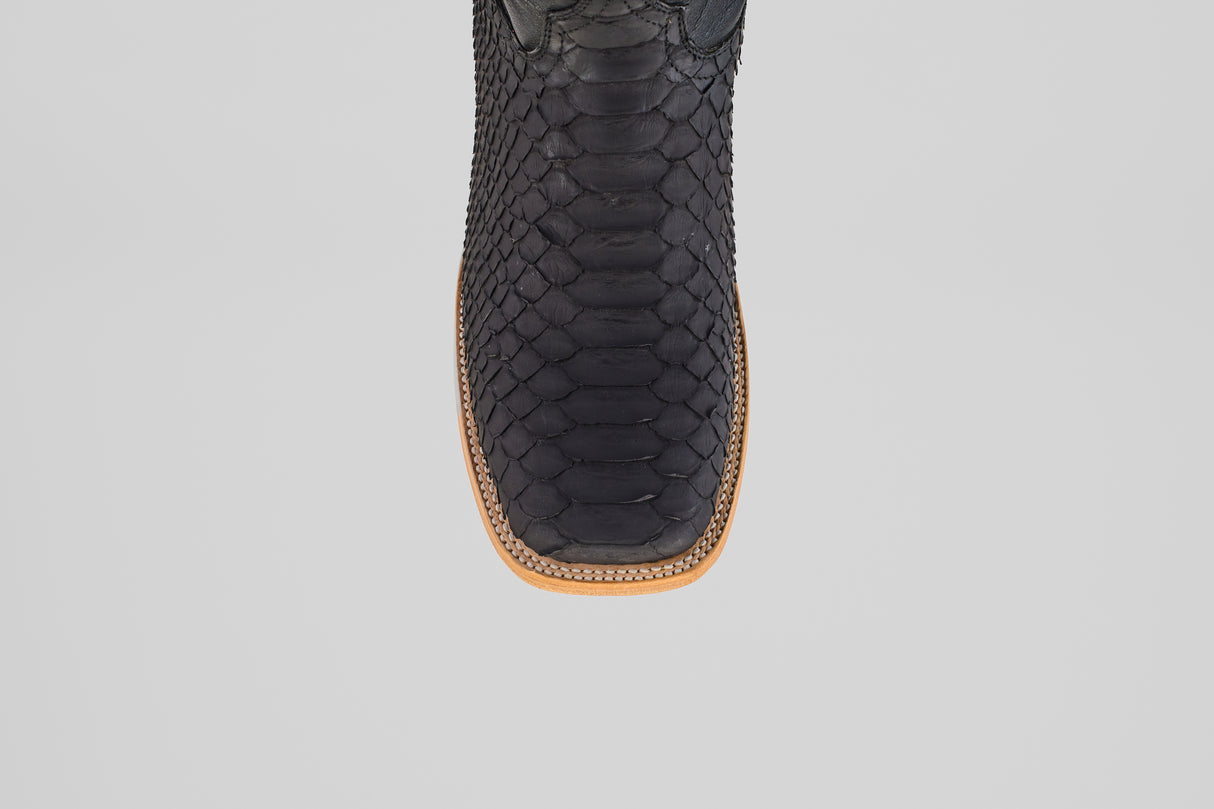 Close-up, top-down view of the toe area of the Wayne - Matte Black - Square Toe boot, featuring matte black snakeskin, a brown leather sole, and decorative edge stitching against a plain light background.