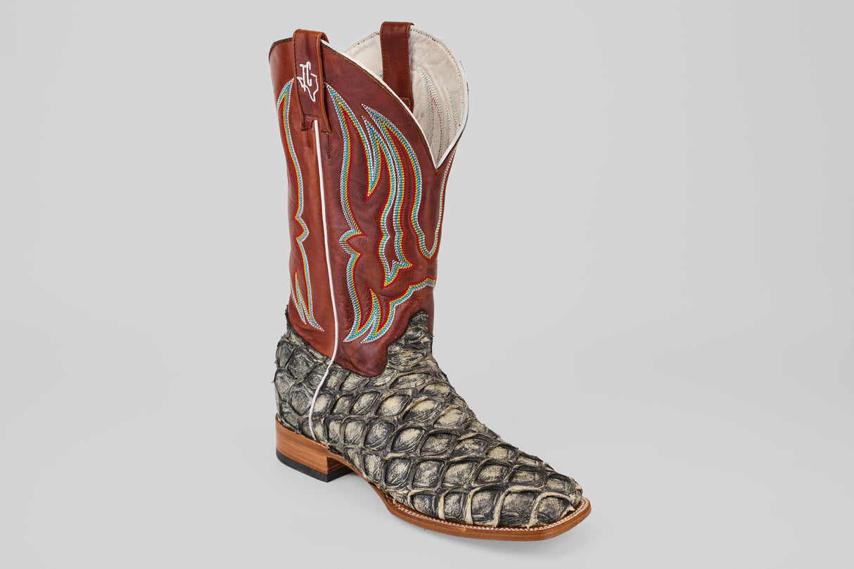 The Robinson - Newspaper - Square Toe is a limited edition cowboy boot with a brown leather upper, colorful stitching, and a grayish-black scale-patterned Purarucu leather lower on a wooden heel, evoking exotic animal skin.