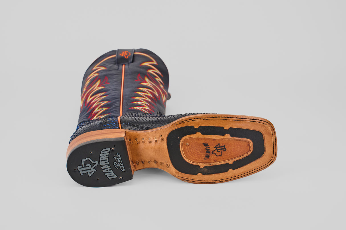 A McGraw - Navy - Square Toe boot from the Diamond Collection lies on its side, displaying a tan leather sole with black rubber heel and logo, plus blue uppers accented by red and yellow flame-like stitching.