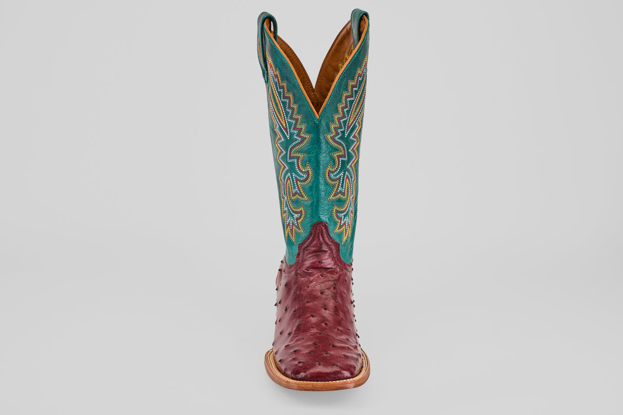 The Rusty - Wine - Square Toe cowboy boot features a wine-hued ostrich leather foot and a tall teal shaft with detailed yellow and white stitching, displayed facing forward on a plain light background.