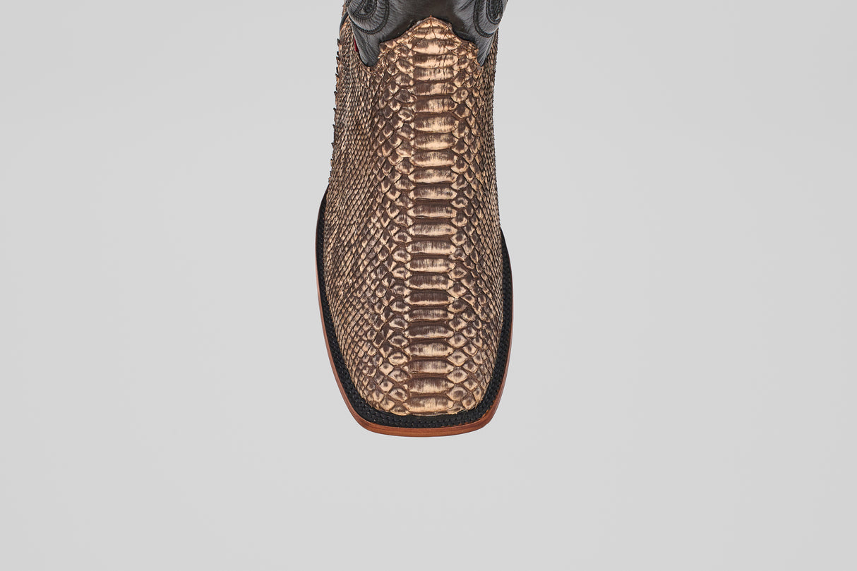 A close-up top view of the Tanner - Rustic Bone - Square Toe boot, featuring brown textured python snakeskin and a square toe, highlights its exotic leather and Western craftsmanship on a light gray background.