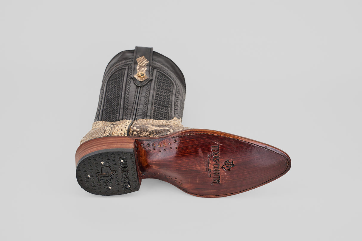 A single Tanner - Natural - Snip Toe cowboy boot rests on its side, featuring a textured black and tan Python Natural H-82 upper and wooden sole with leather finish, branding, and a rubber heel grip. The background is plain light gray.
