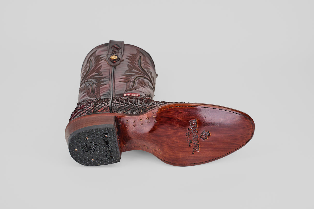 A single Tanner Jumbo - Black Cherry - Round Toe cowboy boot lies on its side, highlighting the decorated shaft, smooth cherry-colored sole with brand logo, and textured heel, set against a plain light gray background.