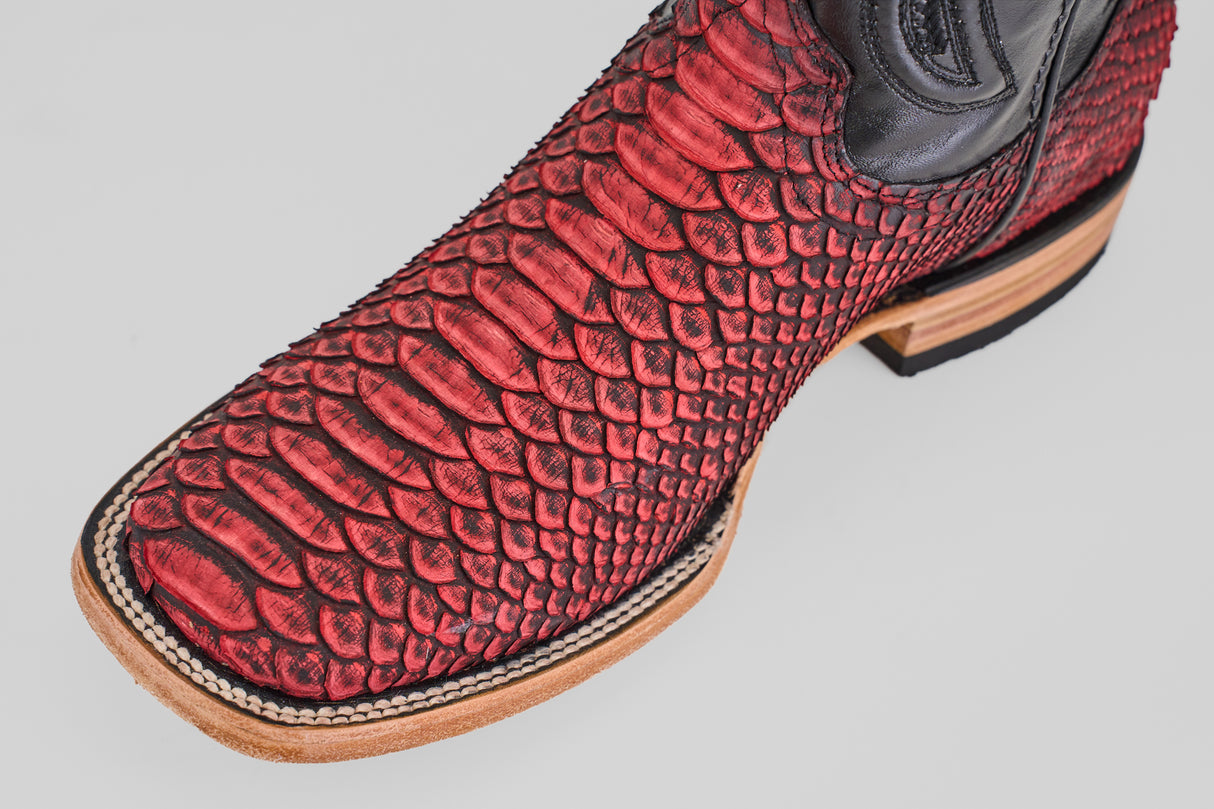 A close-up of the Tanner – Scarlet – Square Toe cowboy boot, featuring red python leather, black accents, and a tan wooden heel and sole, displayed against a plain light background.