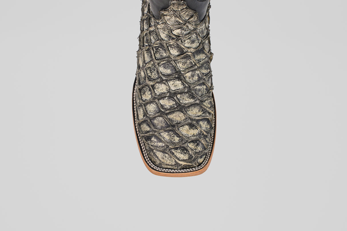 A close-up of the Conor - Rustic Bone - Square Toe men's cowboy boot shows its textured fish leather pattern in brown and tan, with detailed stitching along the sole edge.