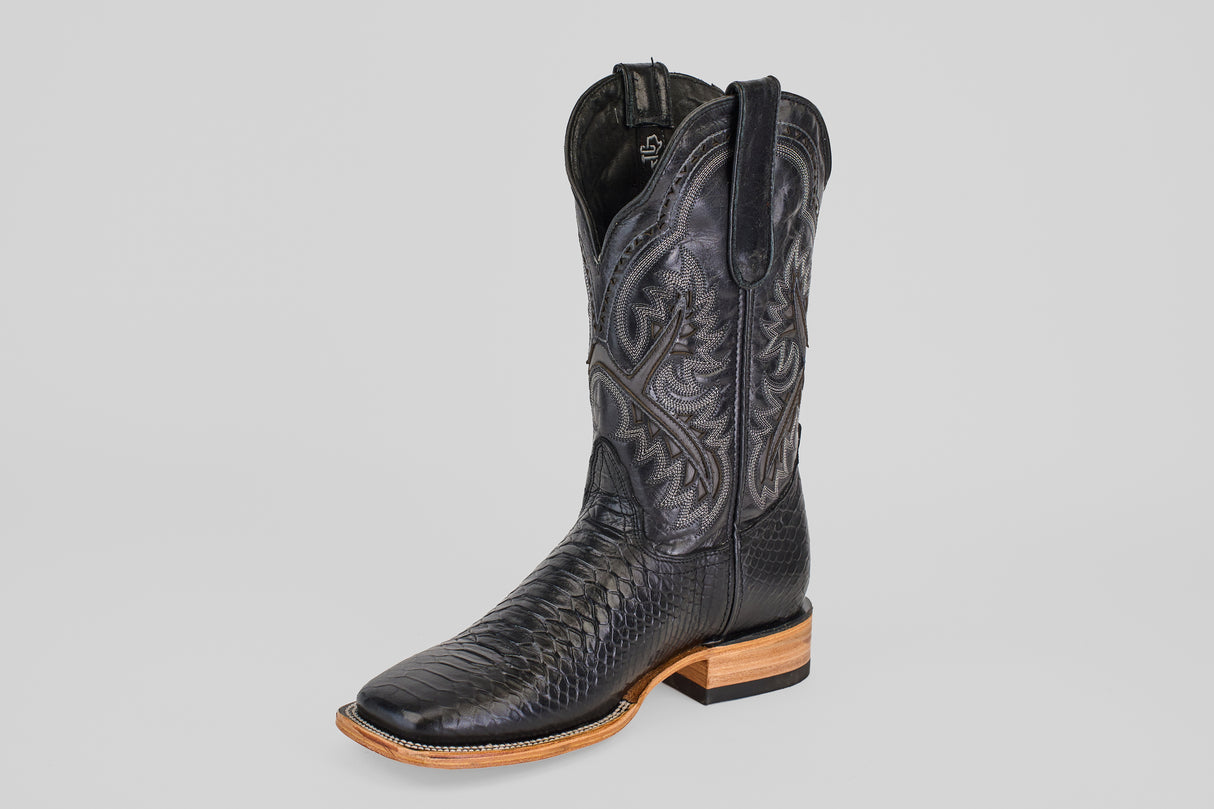 The Python Black - Embossed Leather - Square Toe (E425) is a single black cowboy boot featuring intricate stitching, a textured lower pattern, and a light brown wooden sole, photographed against a plain gray background.