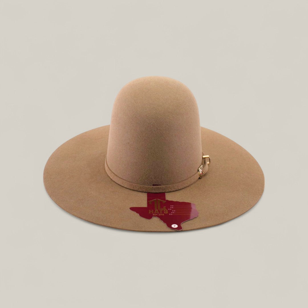 The 10x - Natural - TC Hats is a wide-brimmed, light brown felt western hat with a gold buckle on the band. A maroon Texas-shaped Mr. Hats sticker is attached to the brim, set against a light beige background.