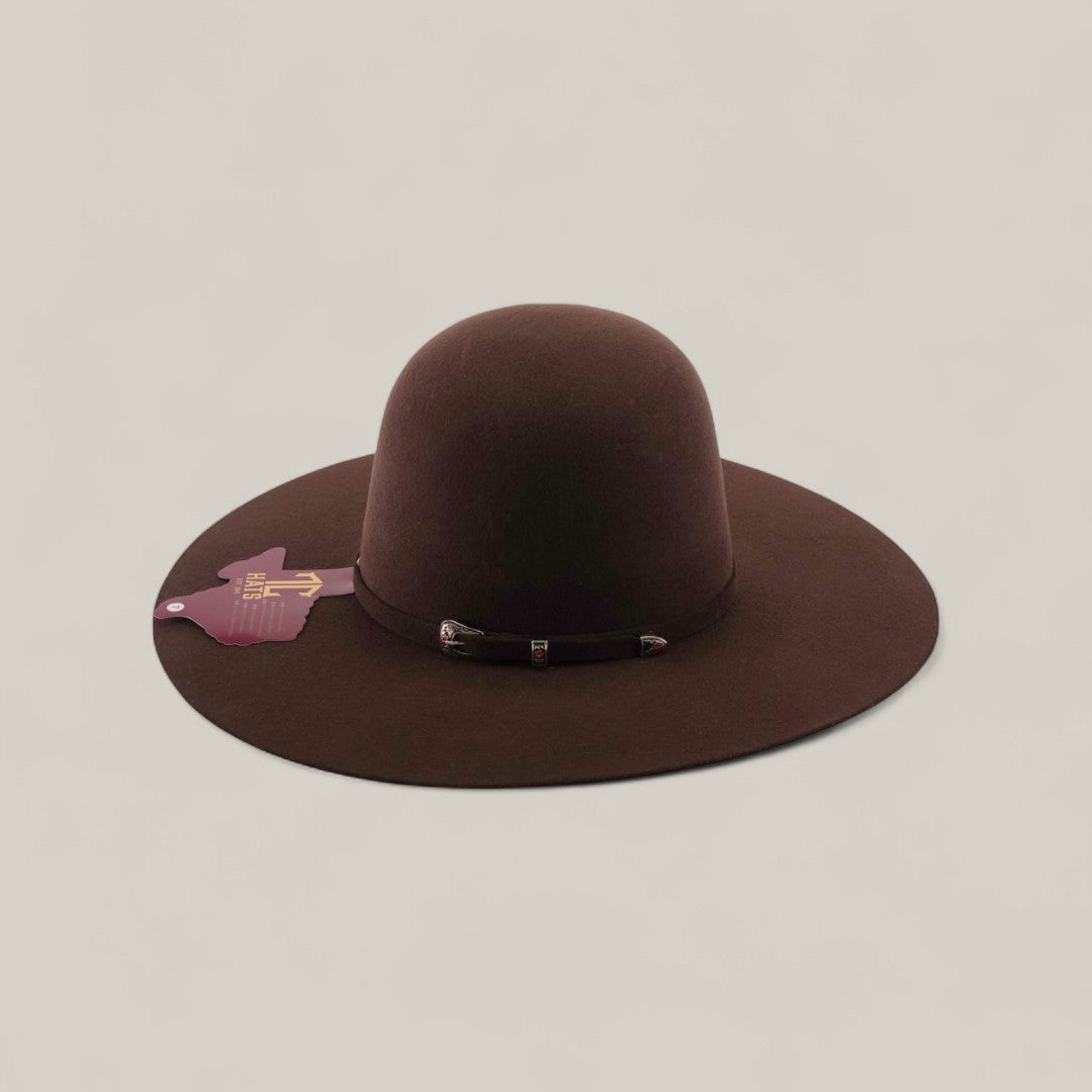 The 4X - Chocolate - TC Hats is a wide-brimmed brown Western felt hat with a rounded crown and decorative band, displayed on a light beige background. A purple cowboy hat-shaped tag is attached to the left brim.