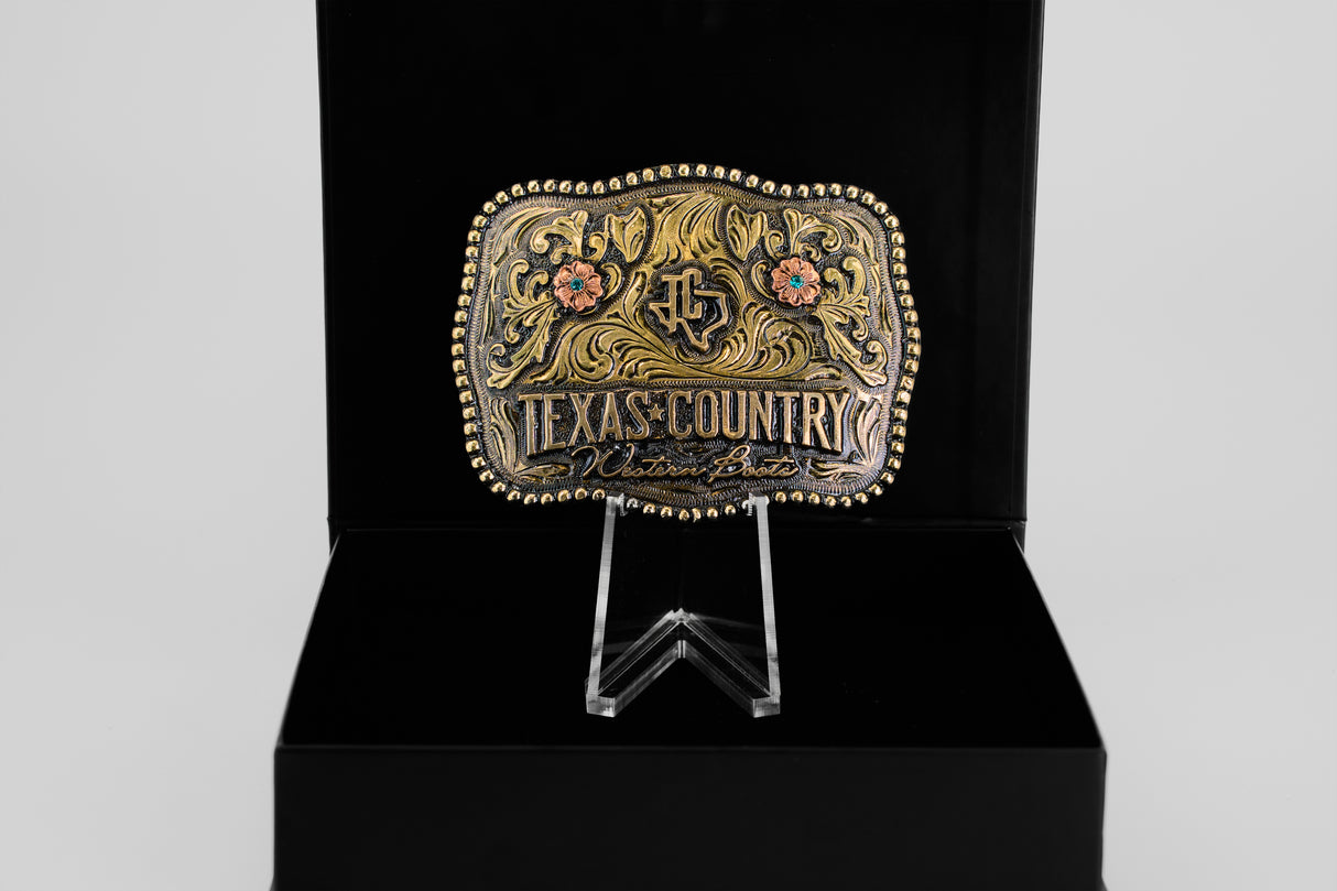The Texas Country Buckle - Mod 3 features floral designs and gold accents, displayed upright in a black box—an eye-catching piece ideal for Western belt buckle collectors.