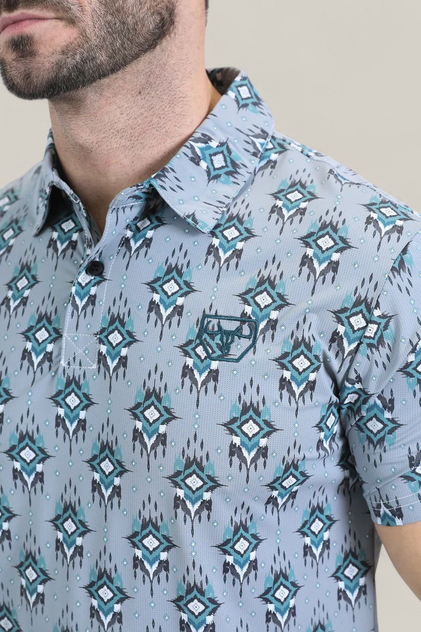 A man with a short beard wears the Mens Performance Fabric Modern Fit Stretch Aztec Print Blue Polo (PGP10871) featuring teal, black, and white Aztec patterns. Only his upper torso and lower face are visible.