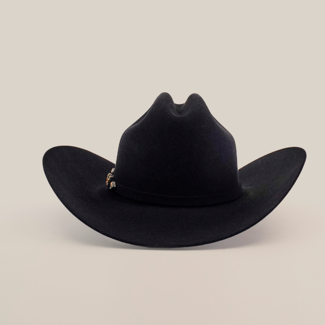 The 10X Jerarca Black is a handcrafted black cowboy hat made from fur felt, with a wide brim and distinctive top crease. It features a small decorative band on one side, exemplifying classic western headwear against a plain white background.