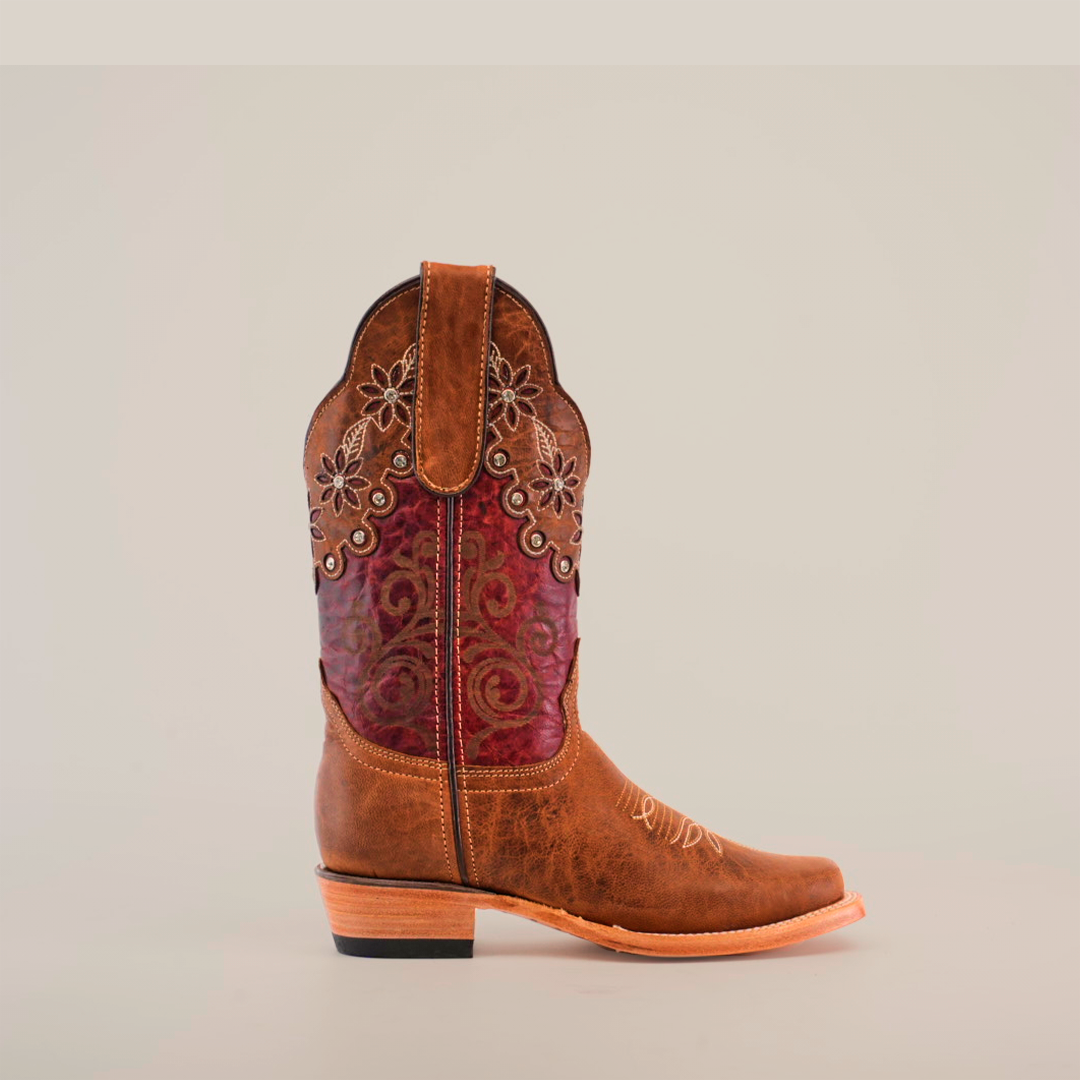 The Grecas Orix - Square Toe boot features premium brown leather, intricate stitching, floral embroidery on the shaft, and a blend of brown and maroon shades for a stylish look. It is paired with a wooden heel and pointed toe, set against a plain white background.