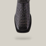 A close-up of the Alligatoar Horn Back Print Black boot showcases exquisite craftsmanship and a crocodile skin pattern on the upper. The square toe design adds modern flair against a light beige background.