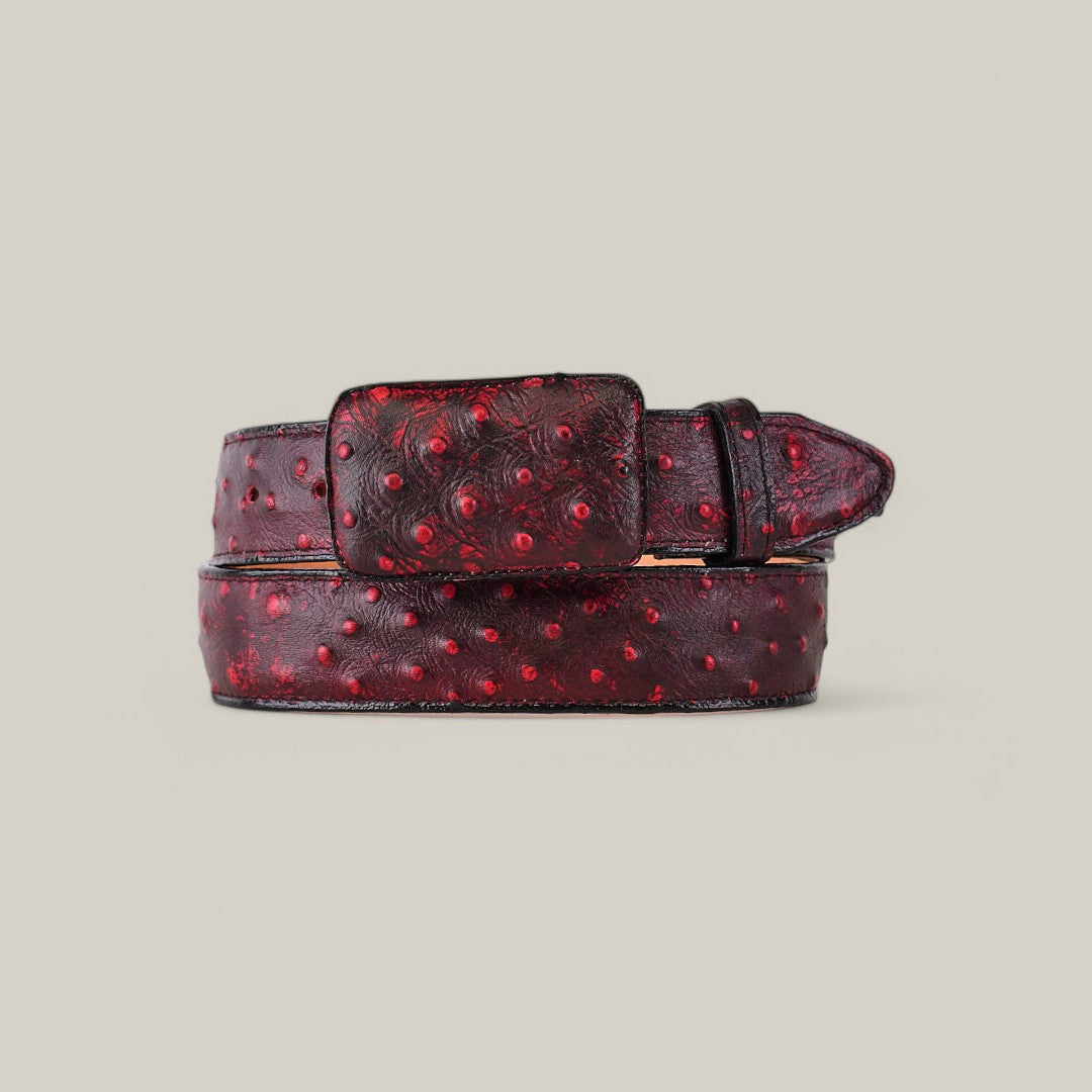 The Ostrich Print Black Cherry Belt features a rich red color with a dimpled texture and a plain light background. It combines elegance with rugged style through its square cowboy buckle and stitched details.