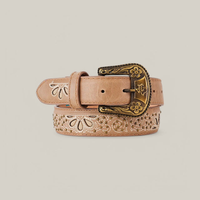 The Sierra Fawn Belt - Texas Buckle features elegant floral carvings on tan leather with a decorative brass buckle, coiled attractively on a beige background, making it an essential women’s wardrobe accessory.