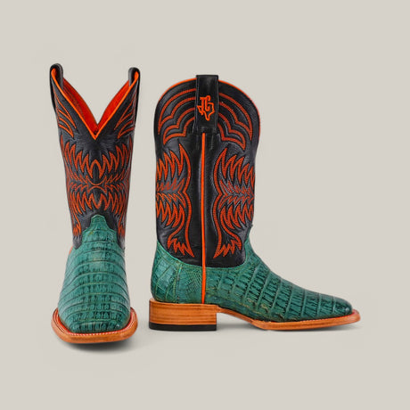 The Exotic Caiman Belly Tail cowboy boots in green boast colorful embroidery and premium caiman leather, featuring intricate red and black designs on the shafts. They have a unique pattern, orange interior lining, and sturdy brown soles.