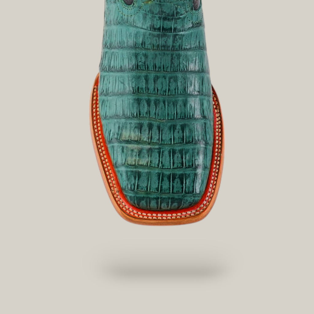 A top view showcases the Exotic Caiman Belly Tail boot in green with a square toe, featuring premium caiman leather. The tan leather sole with red trim and white stitching contrasts against a light gray backdrop, highlighting its exotic pattern.