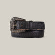 The Python Print Black Belt - Texas Buckle showcases a textured, crocodile-like pattern in black leather, paired with an ornate silver buckle featuring intricate engravings, all set against a plain beige background.