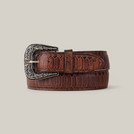 The Python Print Brown - Texas Buckle is a belt with an embossed scale pattern and intricate silver buckle, coiled with the tip through it, set against a gray background for both fashion and function.
