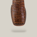 Close-up of the Ross - Orix - Square Toe cowboy boot’s brown, crocodile-patterned toe with detailed stitching, highlighting its quality craftsmanship against a plain beige background.
