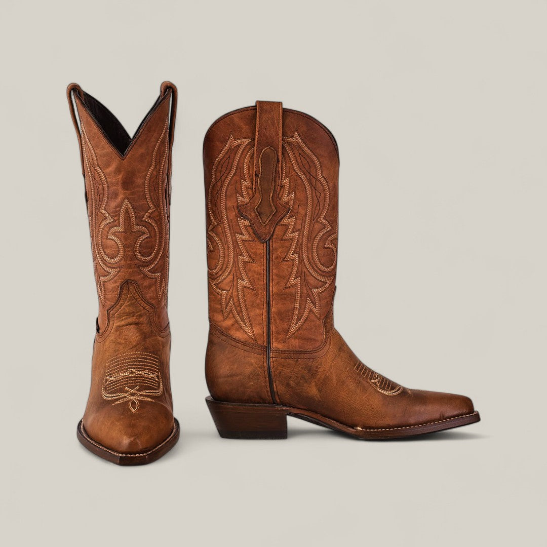 The Fresno - Tabaco - Snip Toe boots in brown cowhide feature decorative stitching; one boot stands upright while the other is angled to display front and side views against a light background, highlighting their quality craftsmanship.