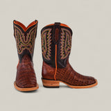 A pair of Exotic Caiman Belly Tail Cognac Kids Boots with a square toe and colorful yellow and orange stitching are displayed, showing the front of one boot and the side of the other, against a neutral background.