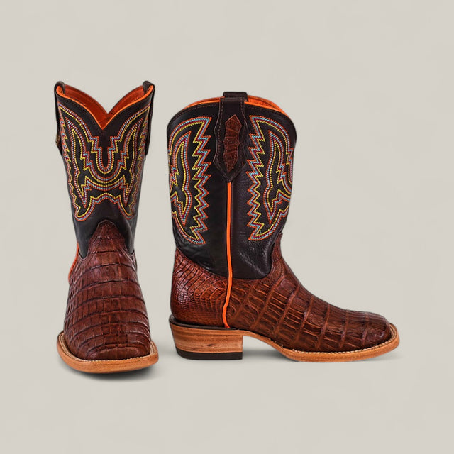 A pair of Exotic Caiman Belly Tail Cognac Kids Boots with a square toe and colorful yellow and orange stitching are displayed, showing the front of one boot and the side of the other, against a neutral background.