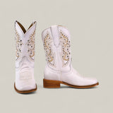 The Amara White - Square Toe - Kids Boots feature light pink leather, intricate tan and white stitching, decorative cutouts, and medium wooden heels for stylish comfort, displayed against a plain beige background.
