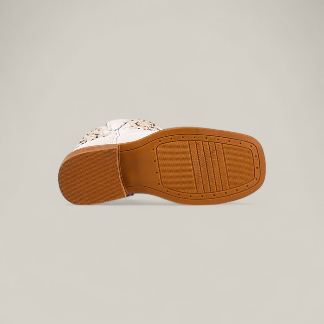 A single Amara White - Square Toe - Kids Boot lies on its side, revealing a tan rubber sole with grip patterns. The premium upper is partly visible against a plain light gray background.