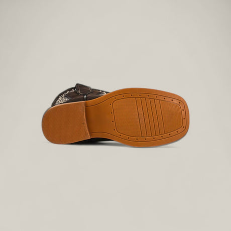 The image shows the sole of the Orion Suede Oxford - Square Toe - Kids Boots in brown suede, featuring a textured pattern and light brown rubber bottom, set against a plain, light-colored background.