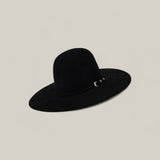 The 10X Grizzly - Tacchino is a wide-brimmed black felt hat with an open, rounded crown and a small decorative metal accent on the band, shown against a plain light beige background.