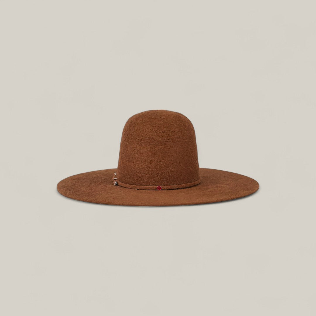 The 10X Grizzly - Tacchino is a wide-brimmed brown felt hat with a rounded open crown, displayed on a beige background. A small charm and red accent on the hatband add luxury to this elegant accessory.