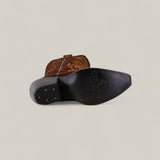 A single Kellie Suede Brownie Leather Sole Tall Shaft Snip Toe boot lies on its side, showing the black sole with gold studs and embossed branding. Decorative stitching accents the leather upper. The background is plain and light.
