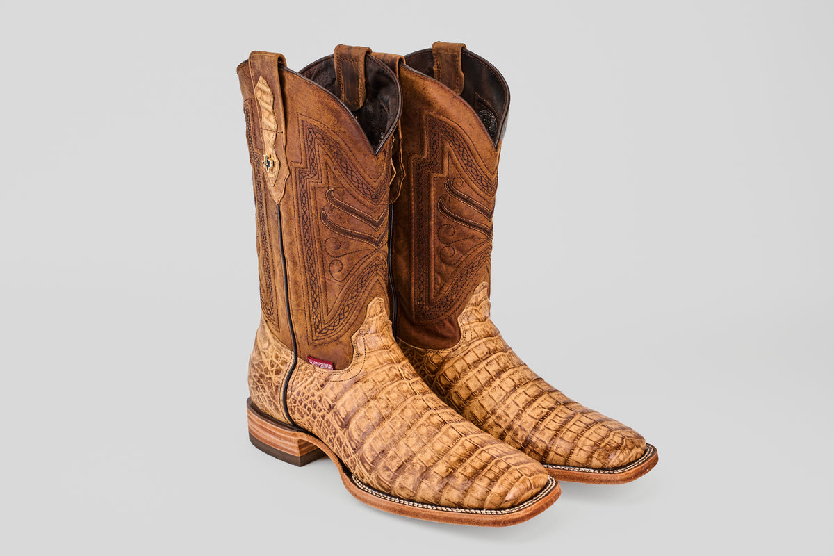 A pair of Exotic Caiman Belly - Antique - Square Toe boots with a brown, crocodile-like textured foot and decorative stitching on the shaft, shown against a plain gray background.