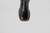 A close-up of the Exotic Caiman Belly - Black- Square Toe boot, featuring crocodile-textured caiman leather and detailed stitching along the tan sole, set against a plain light gray background.