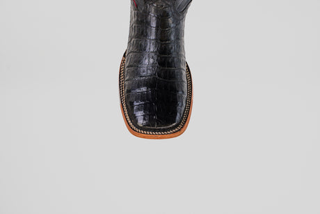 A close-up of the Exotic Caiman Belly - Black- Square Toe boot, featuring crocodile-textured caiman leather and detailed stitching along the tan sole, set against a plain light gray background.