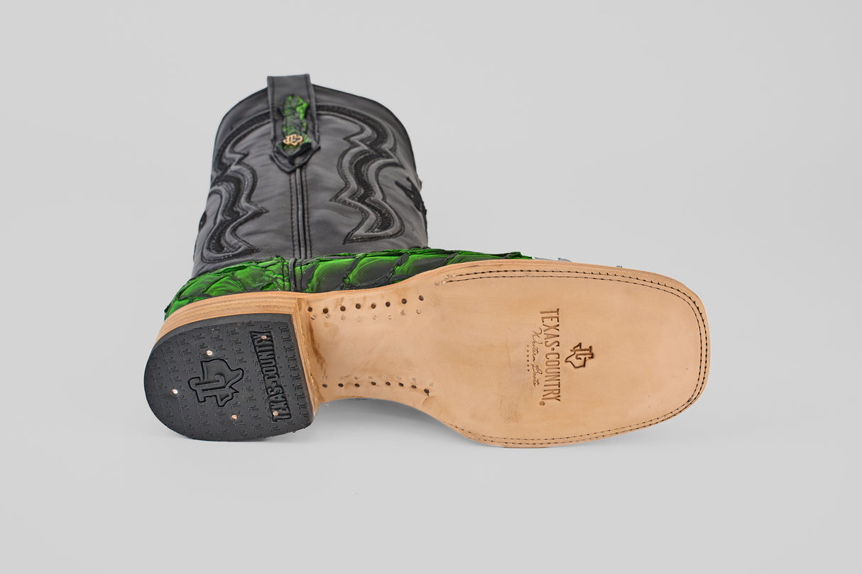 The Conor - Swamp Green - Square Toe boot lies on its side, featuring a black and green design, tan leather sole with Texas Country branding, and a black heel with a Texas-shaped logo—perfect for fans of standout cowboy boots.