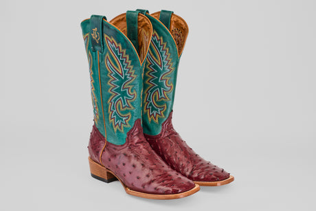 The Rusty - Wine - Square Toe boots feature burgundy wine ostrich feet, a teal shaft with multicolored stitching, light brown soles, and a square toe, showcased against a plain gray background.