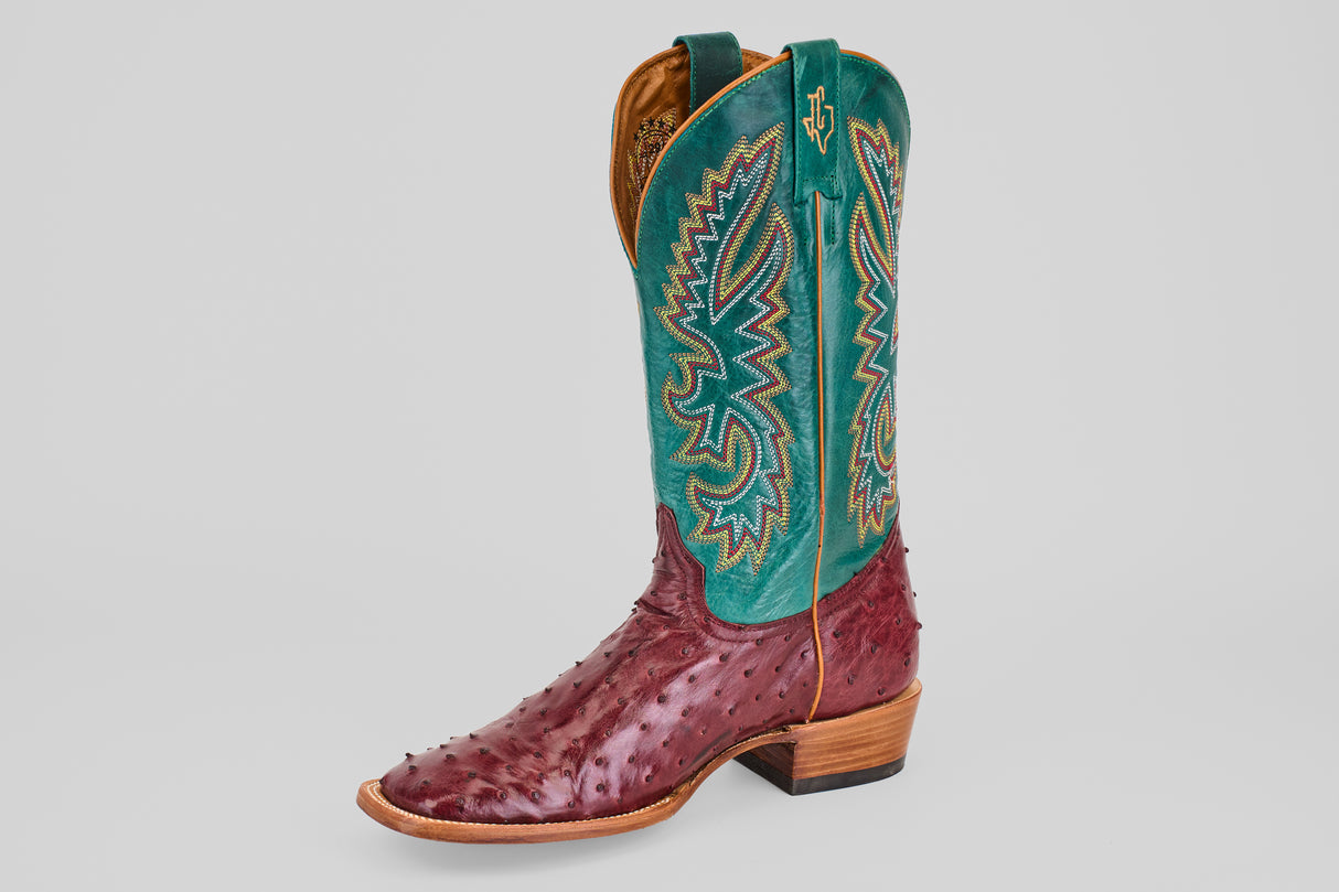 The Rusty - Wine - Square Toe cowboy boot showcases a wine ostrich leather foot, tall teal shaft with detailed yellow, blue, and red stitching, and a wooden heel, all set against a plain white backdrop.