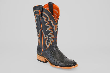 The Steele - Black - Square Toe boot features a black ostrich leather pattern, orange and tan stitching, an orange interior lining, and a light brown wooden heel—luxurious footwear for those seeking standout style.
