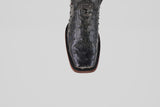 A close-up of the Exotic Ostrich - Black - Rodeo Toe boot shows its textured leather, square toe, and detailed stitching along the brown sole, exemplifying classic western style against a plain light gray background.