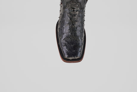 A close-up of the Exotic Ostrich - Black - Rodeo Toe boot shows its textured leather, square toe, and detailed stitching along the brown sole, exemplifying classic western style against a plain light gray background.