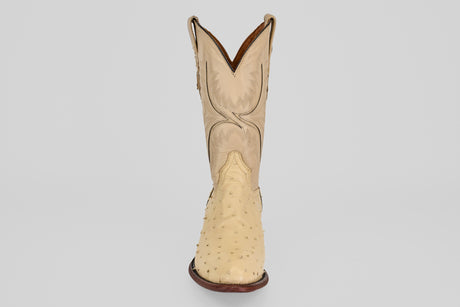 The Exotic Full Quilt Ostrich - Bone features a single genuine ostrich leather cowboy boot in beige with a round toe, decorative shaft stitching, and dark brown sole, displayed facing forward on a plain light background.