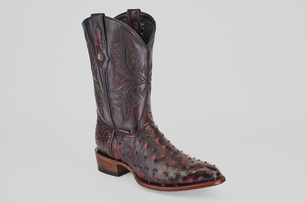 The Exotic Full Quilt Ostrich - Black Cherry - Round Toe is a handcrafted dark brown cowboy boot with Black Cherry red accents, decorative stitching, and ostrich-patterned leather, displayed on a plain light gray background.
