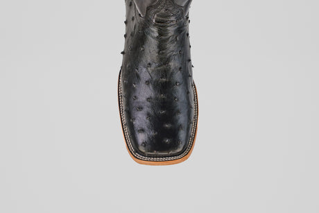 A close-up of the Austin - Black - Square Toe cowboy boot showcases its black avestruz leather, square toe, textured surface, and visible stitching along the light brown sole against a plain light background. Model: AV20 Negro.