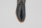 Overhead view of the Austin Leg - Black - Roper Toe boot featuring shiny black ostrich leather with a textured finish and a light brown sole, displayed on a plain light gray background.